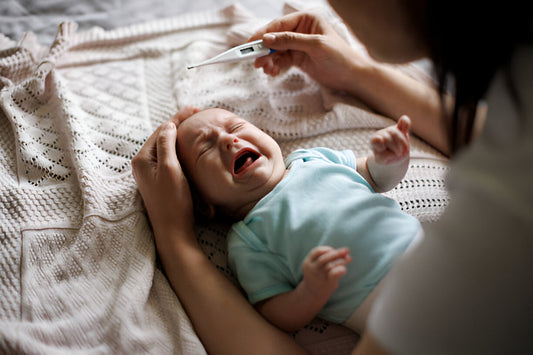 Mamá con termómetro en mano checando la temperatura de su bebé pequeño quien está llorando porque tiene fiebre