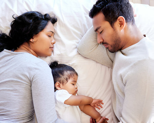 Niña Bebé durmiendo en la cama con papá y mamá