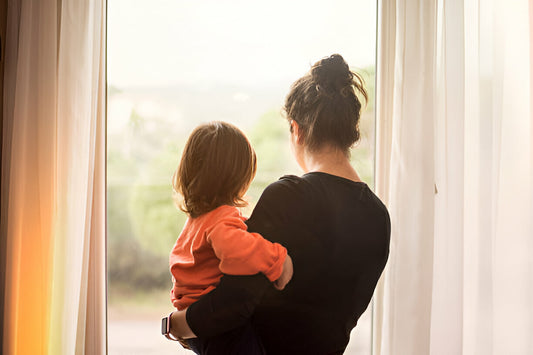 Mamá joven cargando a su hijo mientras ambos miran por la ventana