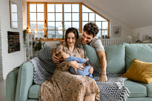 Papá y Mamá viendo a su bebé sentados en un sillón de una casa linda